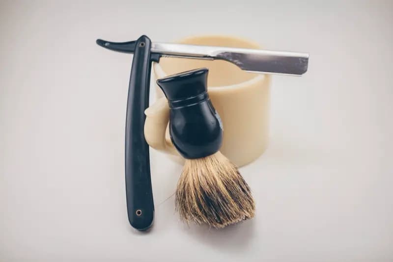 Navalha e pincel de barba apoiados numa tigela clara